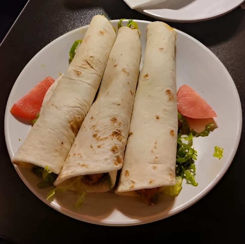 Three African wraps with lettuce and two watermelon slices on a white plate.