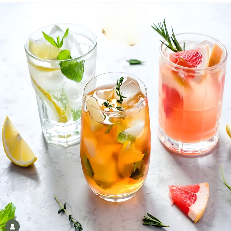Three refreshing cocktails with ice, garnished with mint, thyme, lemon, grapefruit, and rosemary.