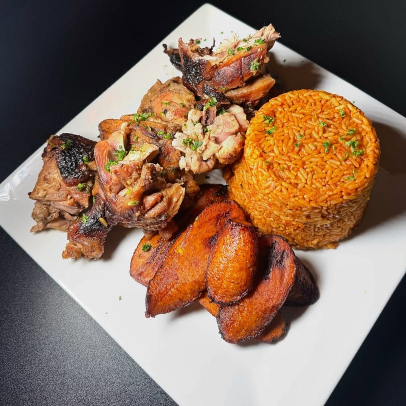 African jollof rice, grilled meat, and fried plantains on a white plate.