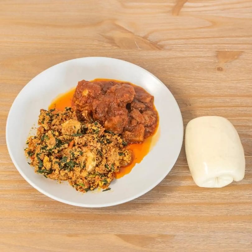 A plate of African egusi soup with meat stew and a side of fufu on a wooden table.