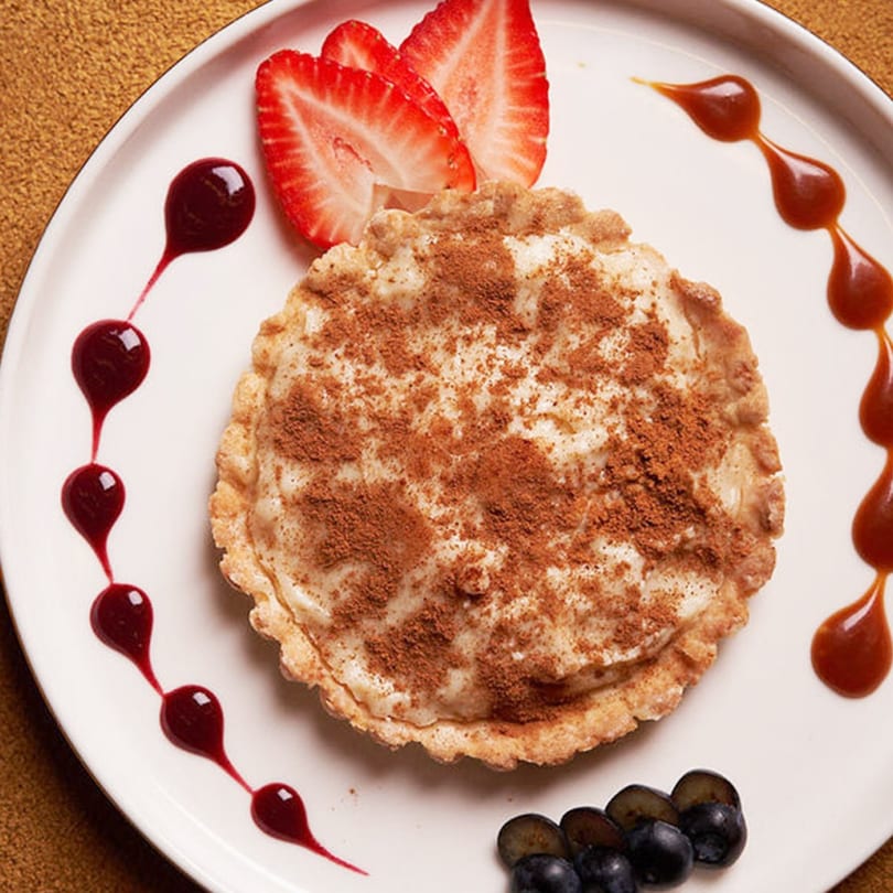 A dessert tart with cinnamon, strawberries, grapes, and berry and caramel drizzles on a white plate.