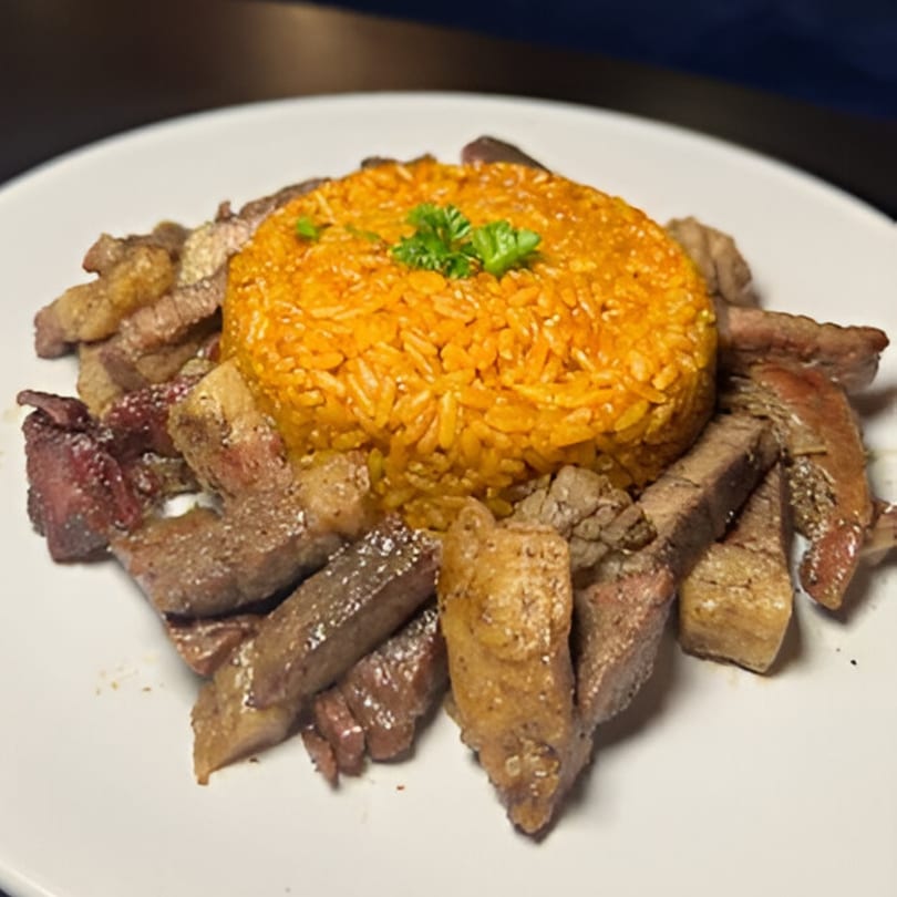 African jollof rice with parsley garnish, surrounded by sliced grilled beef on a white plate.